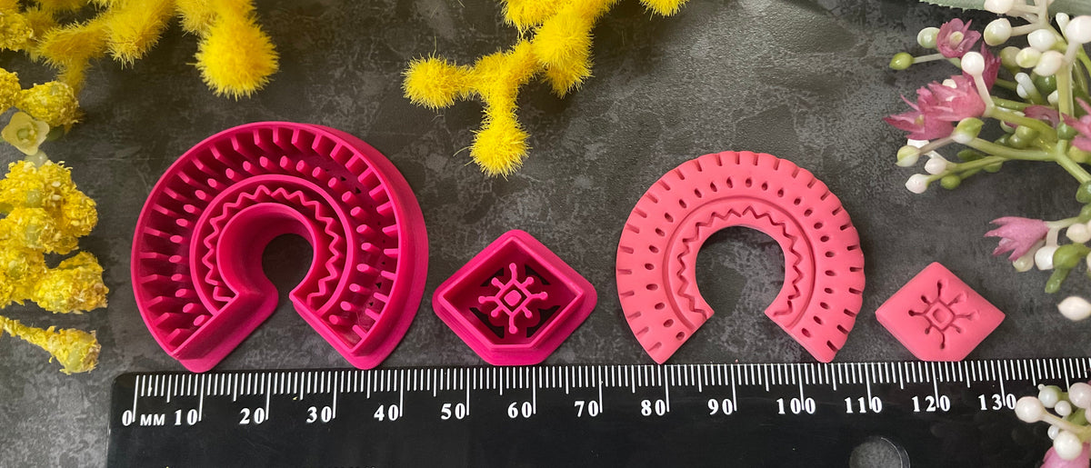 3d printed bright pink polymer clay cutters in different sizes arranged on a dark textured surface, surrounded by decorative yellow and white flowers. Desert Arch Polymer Clay Cutter Set