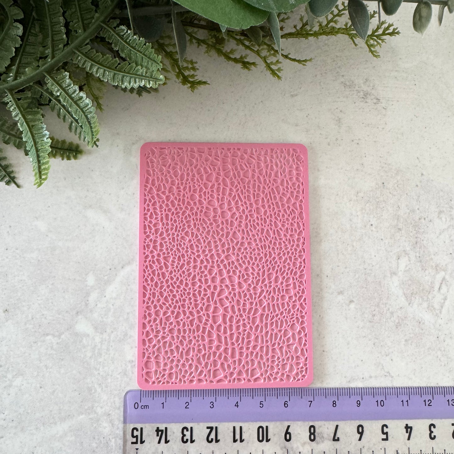 Pink textured card on a light gray surface with green leaves