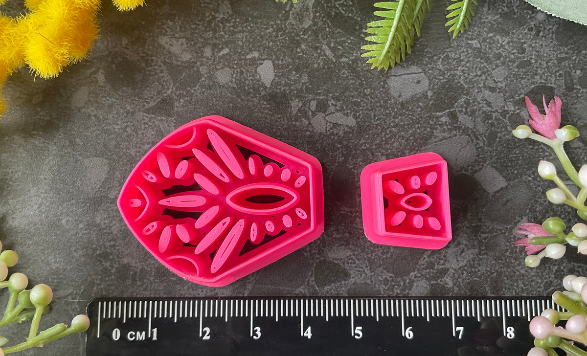 Bright pink3d printed polymer clay cutters in different sizes arranged on a dark textured surface, surrounded by decorative flowers and greenery. Terracotta Tale Polymer Clay Cutter Set