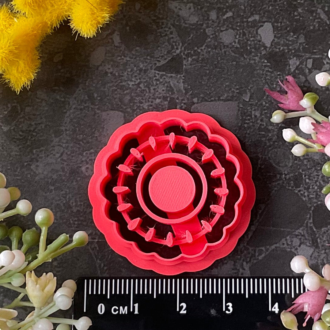 A floral arrangement flat-lay featuring yellow mimosa, white and pink baby's breath flowers, green leaves, and a red circular polymer clay cutter Watermelon Flower Bezel Polymer Clay Cutter Set placed on top of a black ruler on a dark gray textured surface.