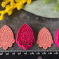 Three teardrop-shaped polymer clay cutters in hot pink and two shades of coral, arranged on a dark gray textured surface with decorative yellow and pink flowers. Afterglow Drop Polymer Clay Cutter