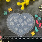 A heart-shaped clear plastic mold with embossed leaf patterns, displayed on a dark textured surface with a black ruler for scale and surrounded by colorful faux flowers.