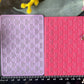 Two textured rectangular cards or texture mats in a bamboo weave pattern, one light lavender and one coral pink, displayed side-by-side on a dark surface with a black measuring ruler at the bottom and yellow and pink flowers framing the scene.
