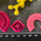 3d printed bright pink polymer clay cutters in different sizes arranged on a dark textured surface, surrounded by decorative yellow and white flowers. Desert Arch Polymer Clay Cutter Set
