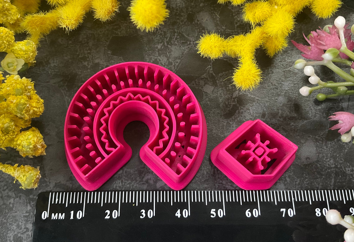 3d printed bright pink polymer clay cutters in different sizes arranged on a dark textured surface, surrounded by decorative yellow and white flowers. Desert Arch Polymer Clay Cutter Set