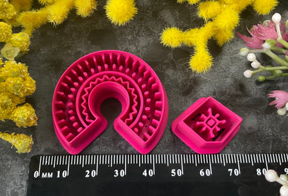 3d printed bright pink polymer clay cutters in different sizes arranged on a dark textured surface, surrounded by decorative yellow and white flowers. Desert Arch Polymer Clay Cutter Set