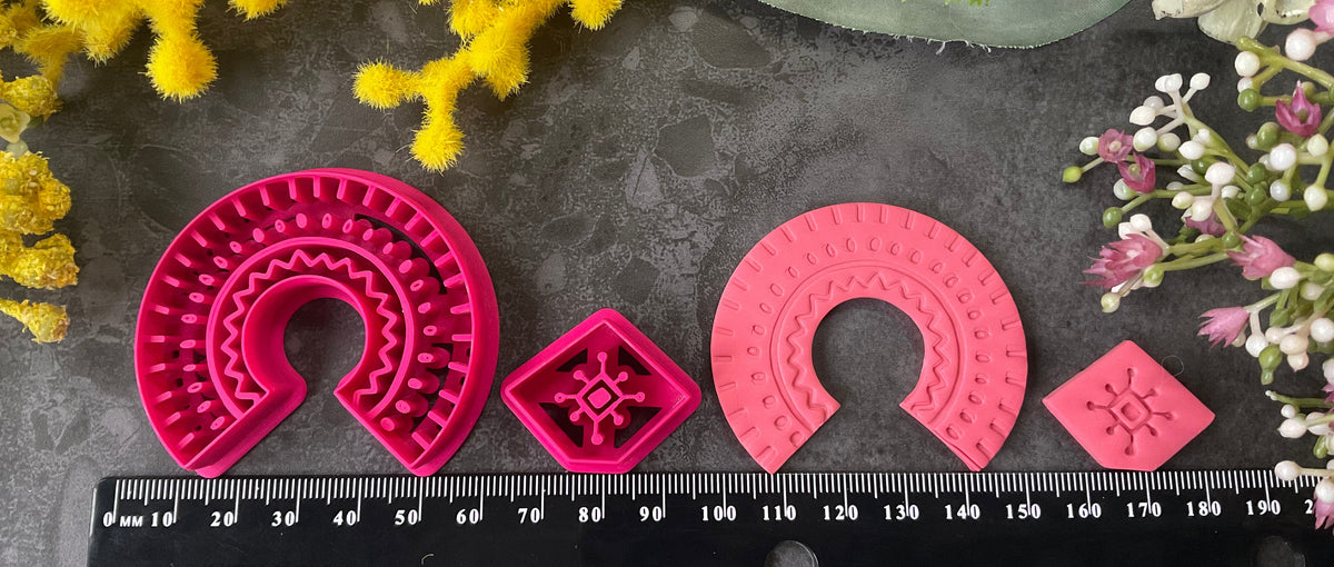 3d printed bright pink polymer clay cutters in different sizes arranged on a dark textured surface, surrounded by decorative yellow and white flowers. Desert Arch Polymer Clay Cutter Set