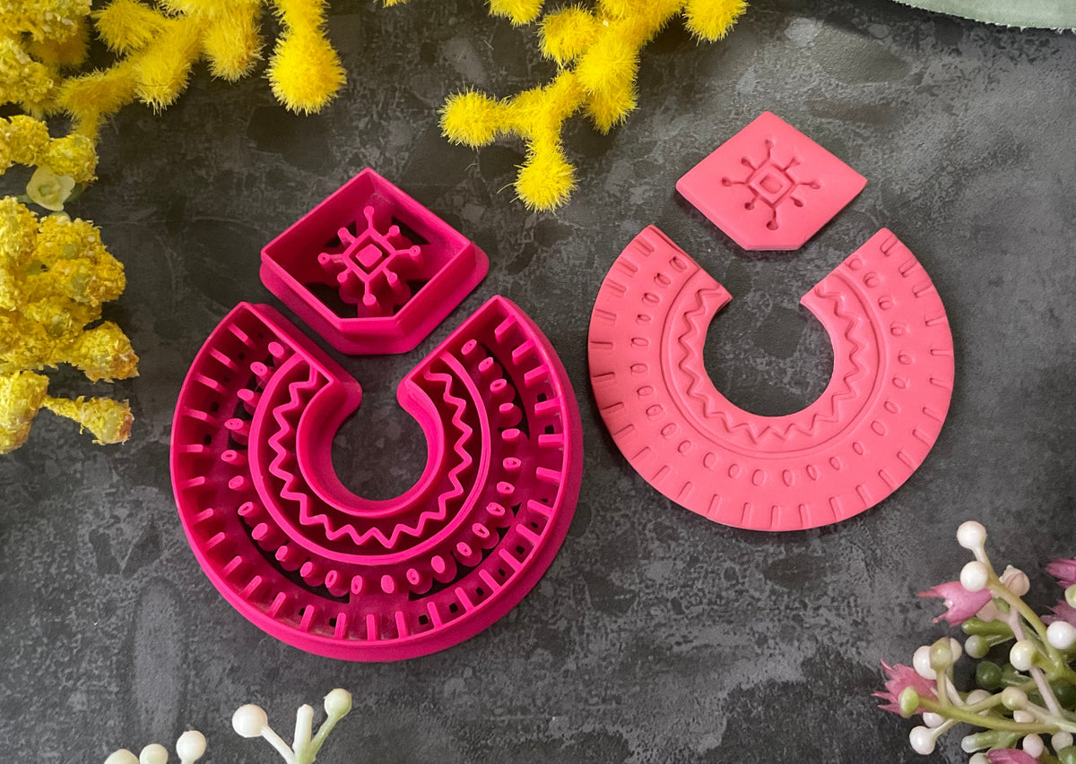 3d printed bright pink polymer clay cutters in different sizes arranged on a dark textured surface, surrounded by decorative yellow and white flowers. Desert Arch Polymer Clay Cutter Set