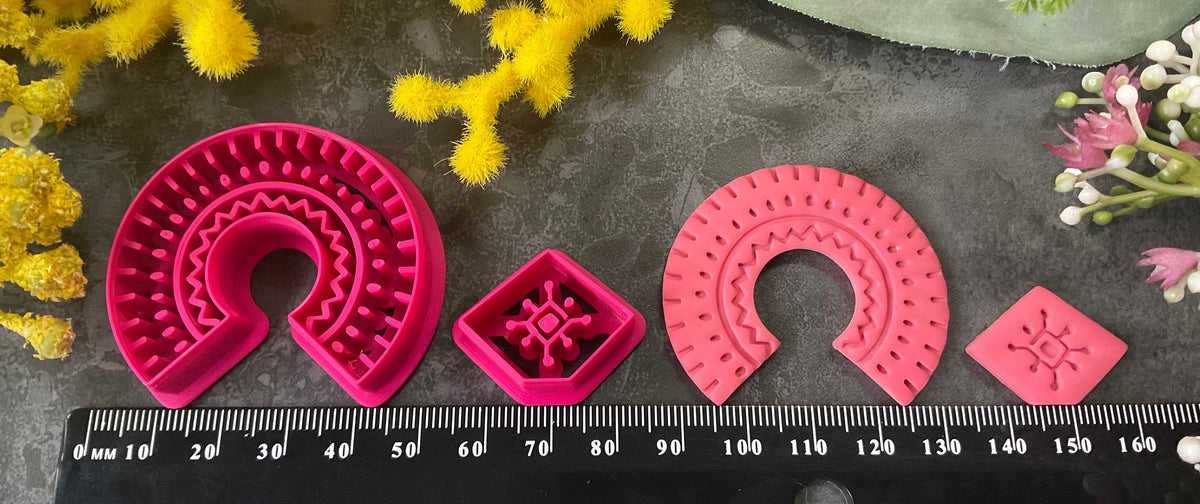 3d printed bright pink polymer clay cutters in different sizes arranged on a dark textured surface, surrounded by decorative yellow and white flowers. Desert Arch Polymer Clay Cutter Set