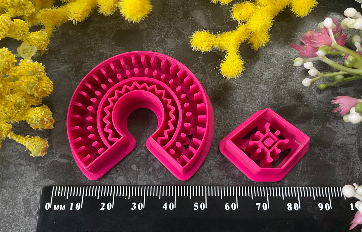 3d printed bright pink polymer clay cutters in different sizes arranged on a dark textured surface, surrounded by decorative yellow and white flowers. Desert Arch Polymer Clay Cutter Set