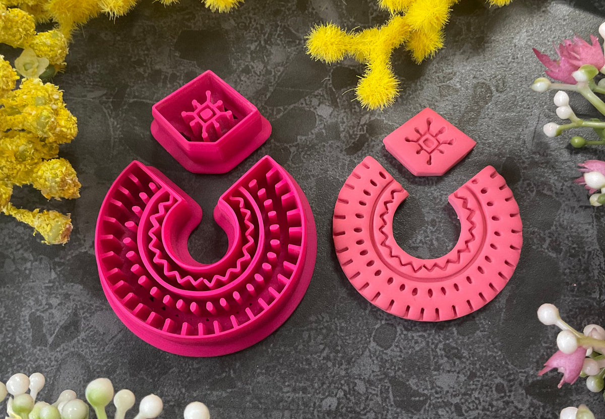 3d printed bright pink polymer clay cutters in different sizes arranged on a dark textured surface, surrounded by decorative yellow and white flowers. Desert Arch Polymer Clay Cutter Set