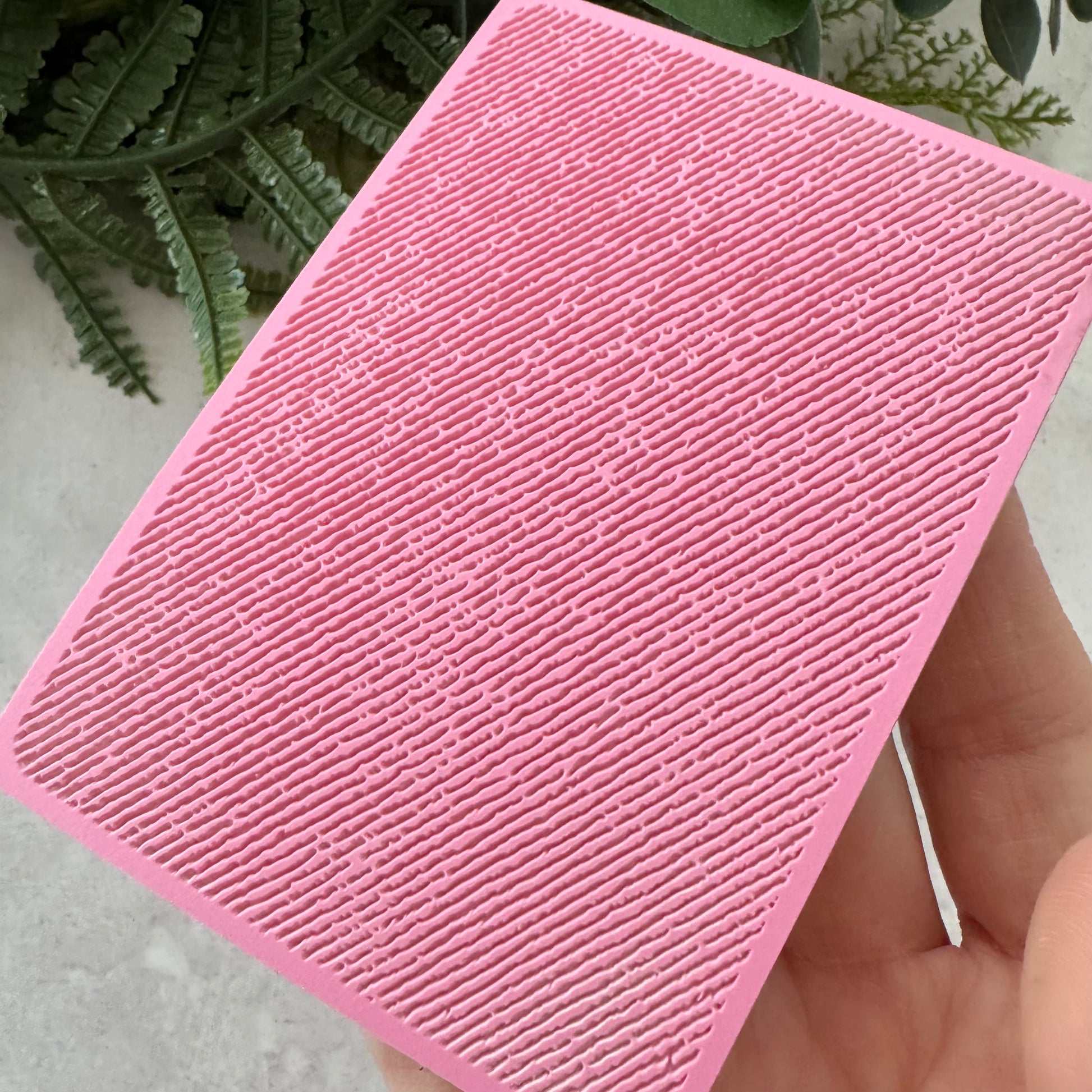 Pink textured square object held by a hand with a natural background