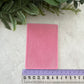 A pink rectangular silicone mold with a textured, ribbed surface, shown on a light gray stone background with a purple ruler at the bottom for scale and green foliage at the top.