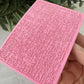 Pink textured card held by a hand with a plant in the background