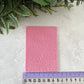 Pink textured card on a light gray surface with green leaves