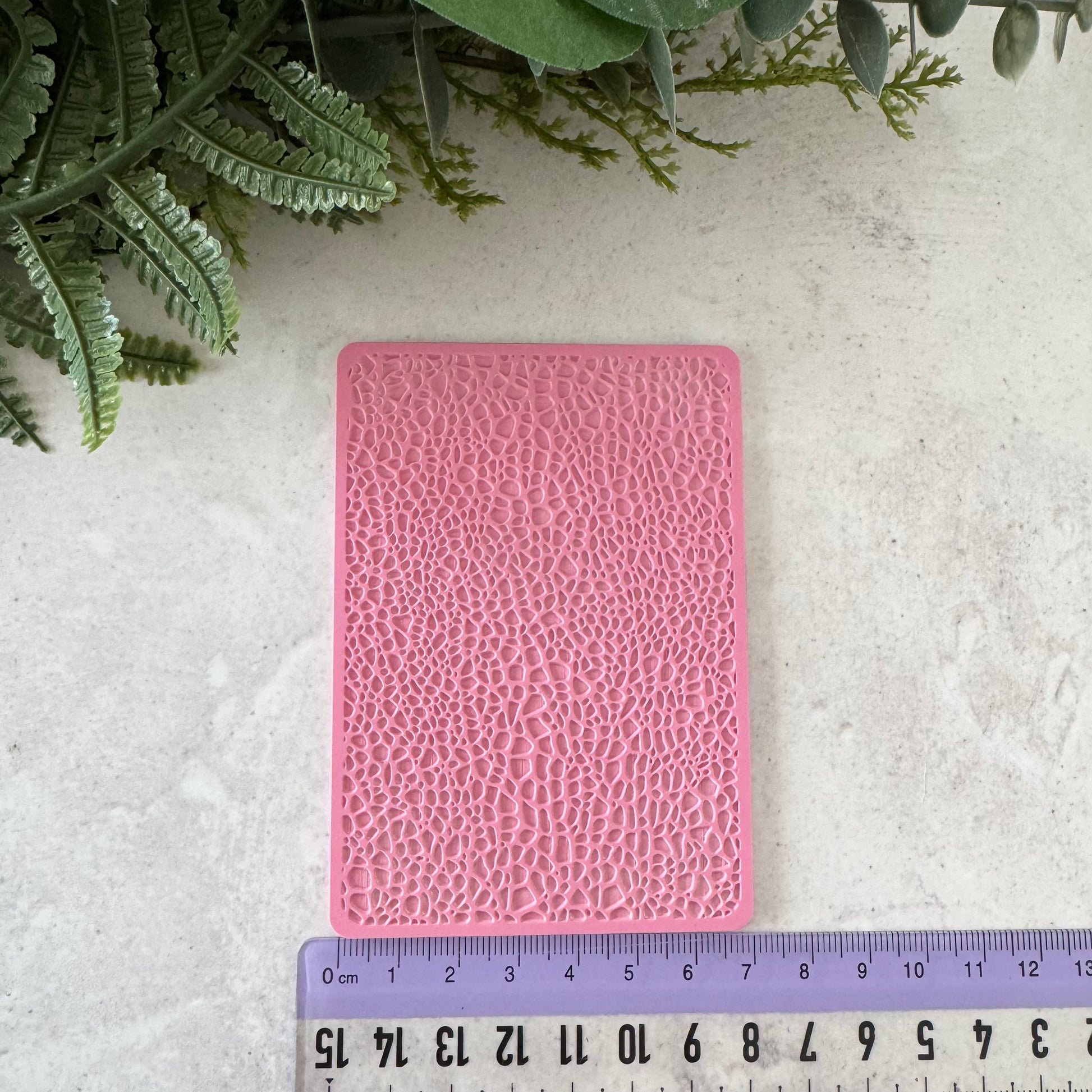 Pink textured card on a light gray surface with green leaves