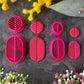 A set of bright pink 3d printed leaf-shaped polymer clay cutters arranged on a dark gray textured surface, surrounded by yellow and pink flowers. Etched Forms Polymer Clay Cutter Set