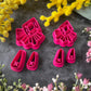 A set of bright pink and turquoise 3d printed polymer clay cutters arranged on a dark textured surface with decorative flowers around the edges. The set includes large fan-shaped stamping cutters, smaller matching cutters, and pointed cone-shaped cutters. First Light Polymer Clay Cutter Set