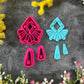 A set of bright pink and turquoise 3d printed polymer clay cutters arranged on a dark textured surface with decorative flowers around the edges. The set includes large fan-shaped stamping cutters, smaller matching cutters, and pointed cone-shaped cutters. First Light Polymer Clay Cutter Set