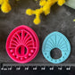 Three 3d printed polymer clay cutters in bright pink, arranged on a dark textured surface surrounded by colorful flowers. Halo Beam Polymer Clay Cutter