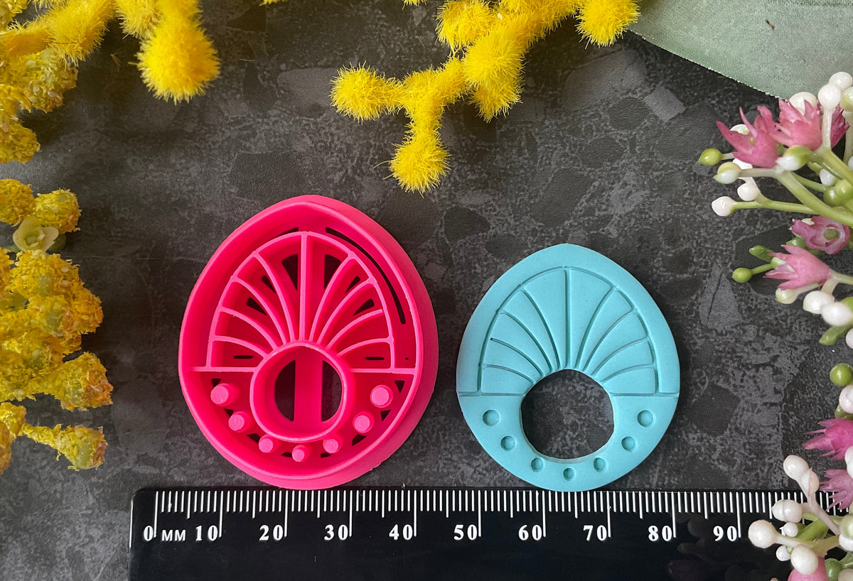 Three 3d printed polymer clay cutters in bright pink, arranged on a dark textured surface surrounded by colorful flowers. Halo Beam Polymer Clay Cutter