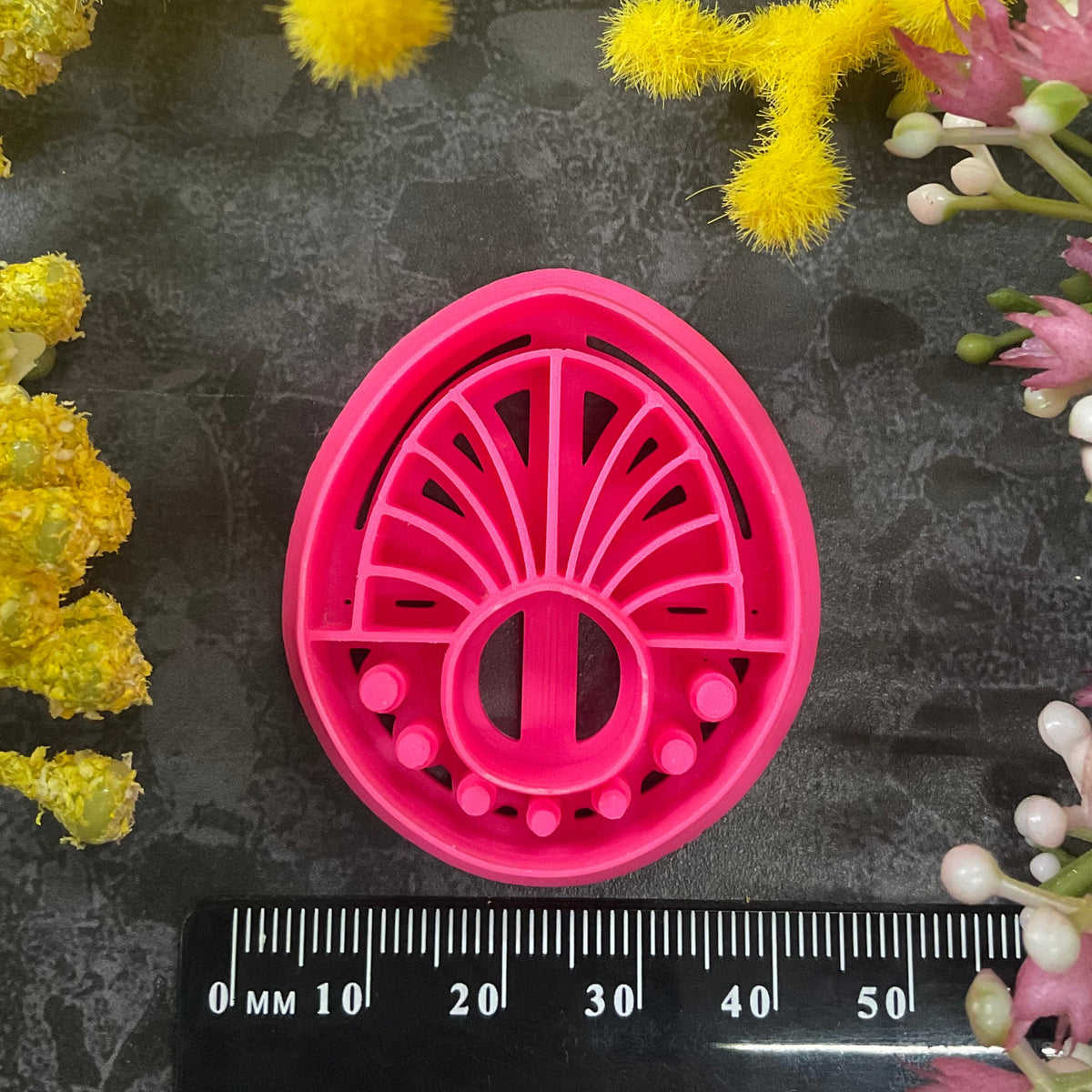 Three 3d printed polymer clay cutters in bright pink, arranged on a dark textured surface surrounded by colorful flowers. Halo Beam Polymer Clay Cutter