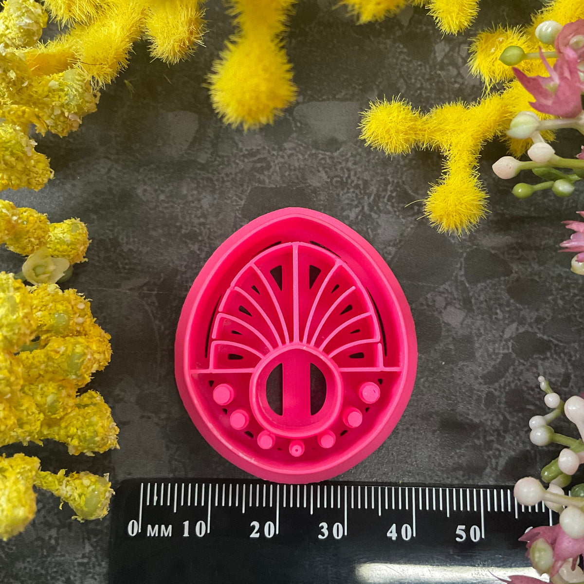 Three 3d printed polymer clay cutters in bright pink, arranged on a dark textured surface surrounded by colorful flowers. Halo Beam Polymer Clay Cutter
