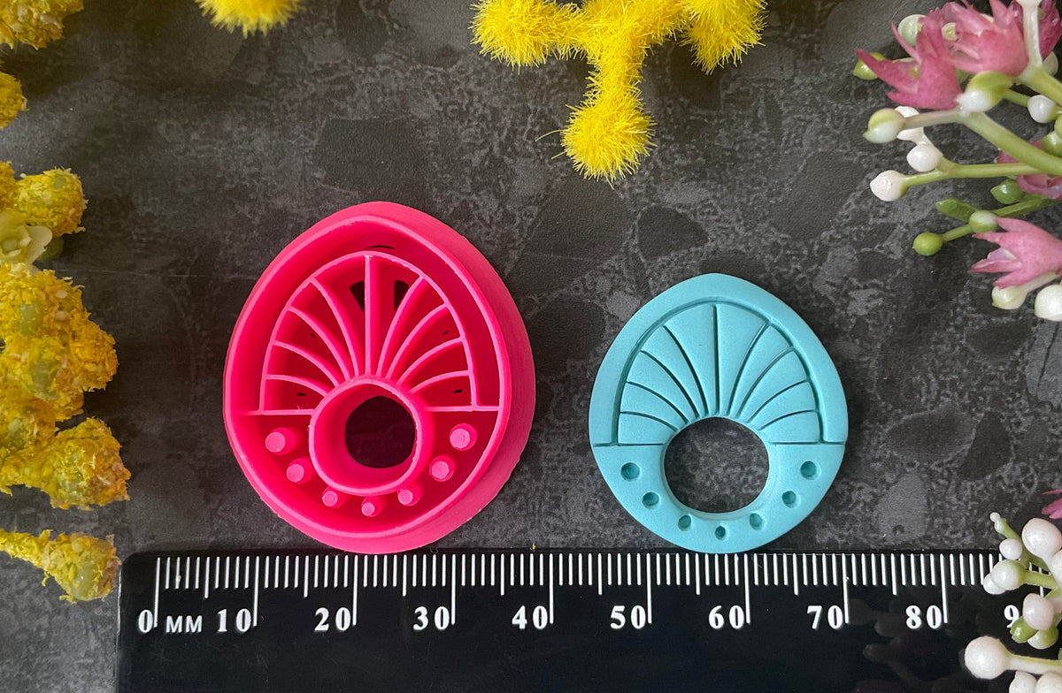 Three 3d printed polymer clay cutters in bright pink, arranged on a dark textured surface surrounded by colorful flowers. Halo Beam Polymer Clay Cutter