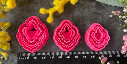 Three hot pink 3d printed polymer clay  cutters arranged on a dark textured surface with decorative flowers around them, set against yellow mimosa and pink/white blossoms. Heirloom Lace Polymer Clay Cutter