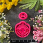 Bright pink 3d printed polymer clay cutters arranged on a dark textured surface, surrounded by decorative flowers and greenery. Morning Ray Polymer Clay Cutter Set