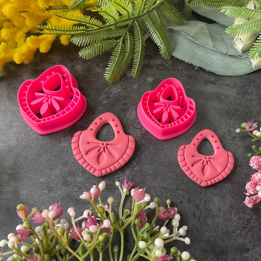 Hot  pink teardrop-shaped polymer clay craft cutters arranged on a dark textured surface with decorative flowers and greenery around them. Nomad Teardrop Polymer Clay Cutter
