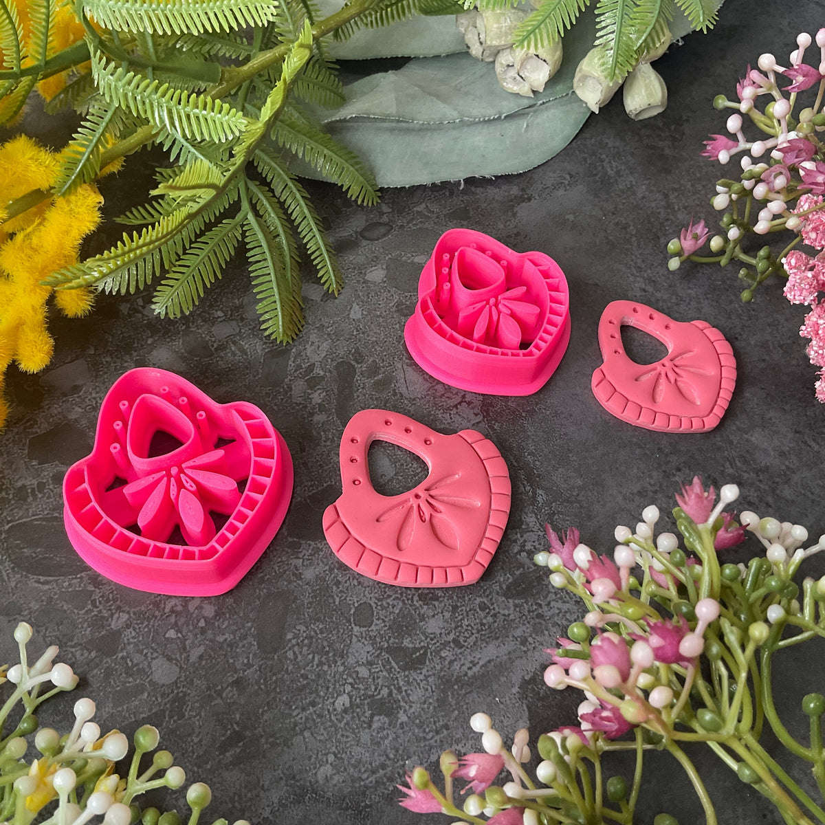 Hot  pink teardrop-shaped polymer clay craft cutters arranged on a dark textured surface with decorative flowers and greenery around them. Nomad Teardrop Polymer Clay Cutter