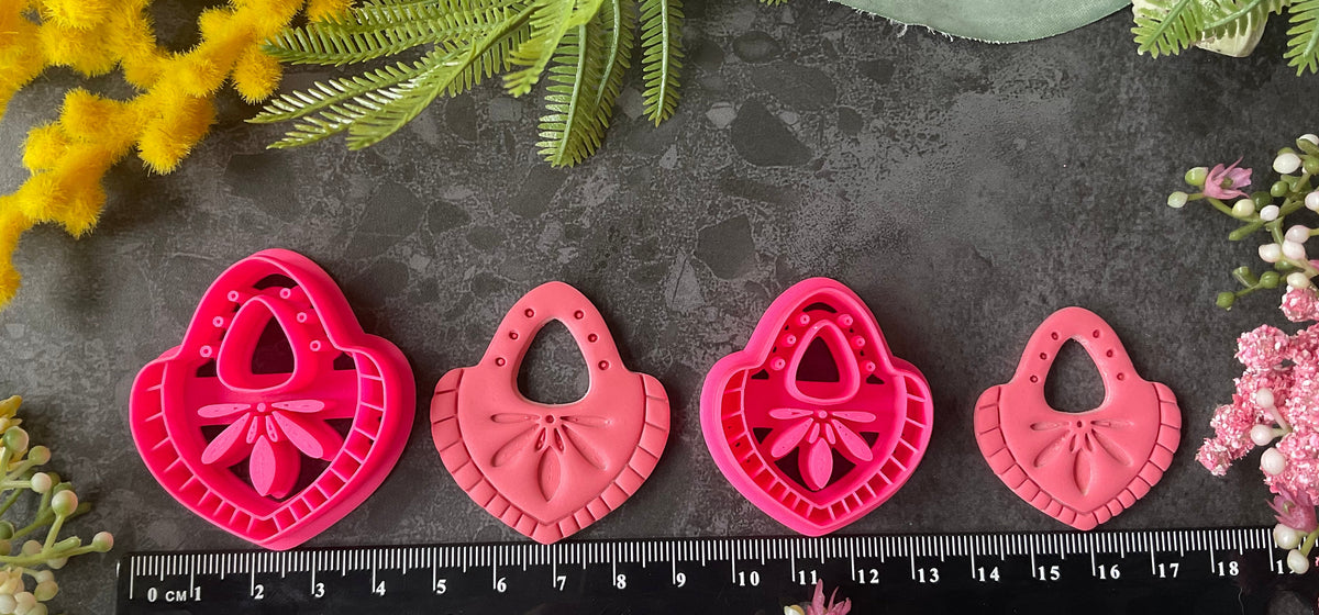 Hot  pink teardrop-shaped polymer clay craft cutters arranged on a dark textured surface with decorative flowers and greenery around them. Nomad Teardrop Polymer Clay Cutter