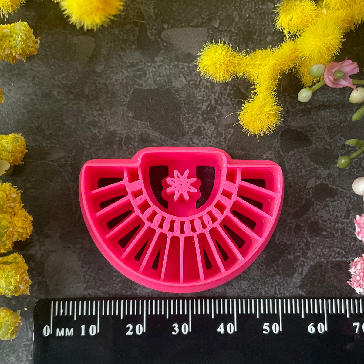 Three pink 3d printed polymer clay cutters arranged on a dark textured surface with decorative yellow and pink flowers around the edges. Palm Fan Polymer Clay Cutter