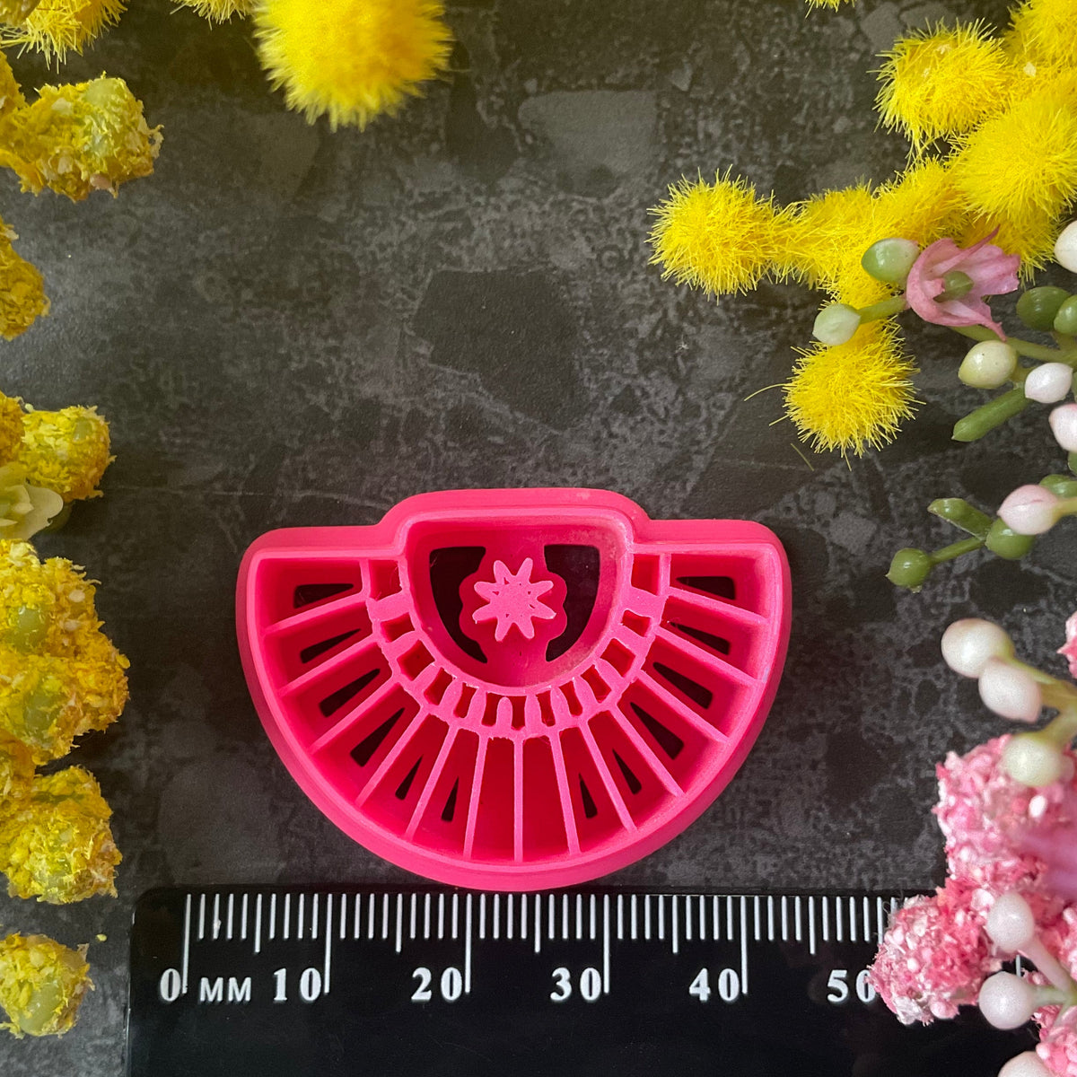 Three pink 3d printed polymer clay cutters arranged on a dark textured surface with decorative yellow and pink flowers around the edges. Palm Fan Polymer Clay Cutter