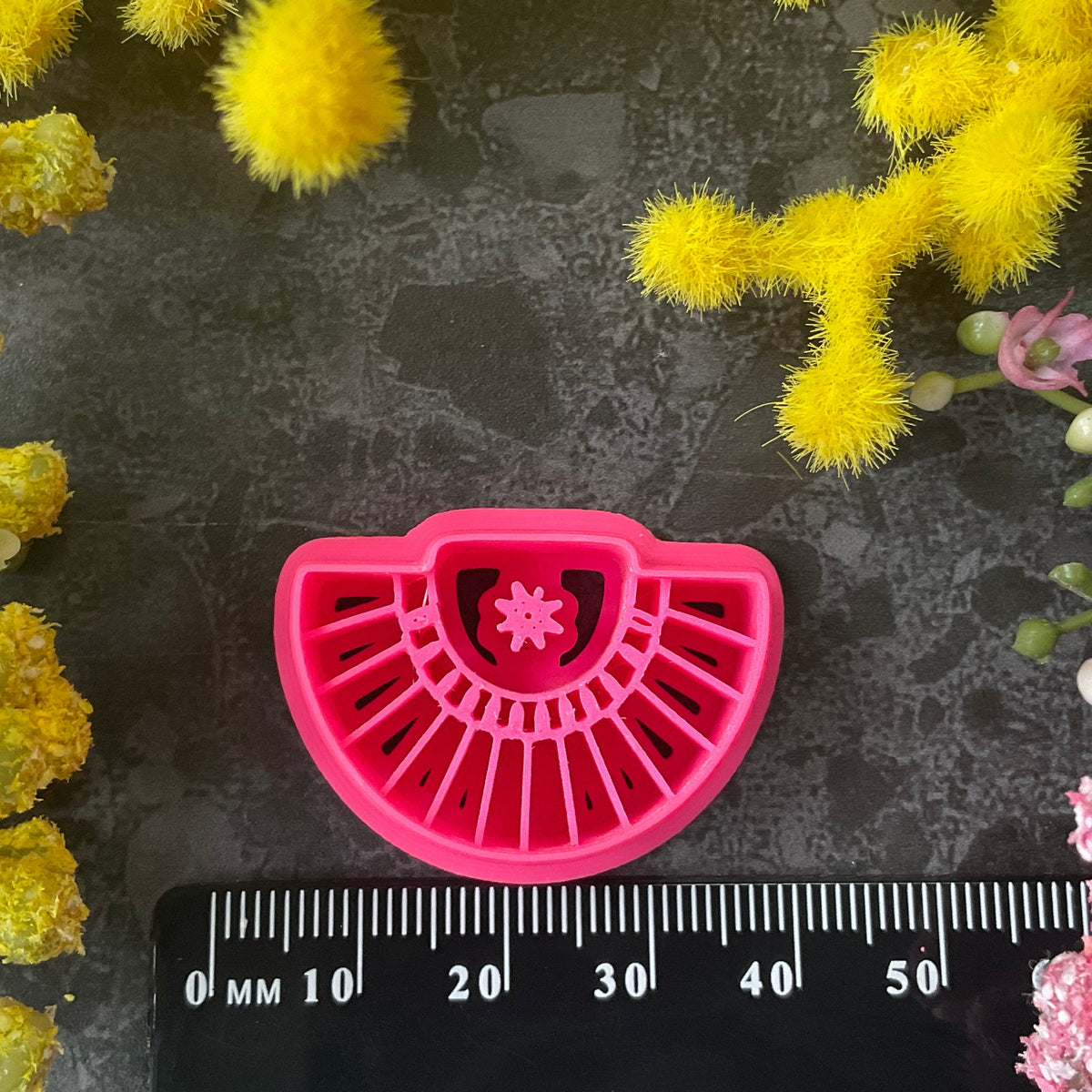 Three pink 3d printed polymer clay cutters arranged on a dark textured surface with decorative yellow and pink flowers around the edges. Palm Fan Polymer Clay Cutter
