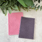 Pink and gray texture mat in the pattern of psychedelic checkerboards on a light surface with green foliage.