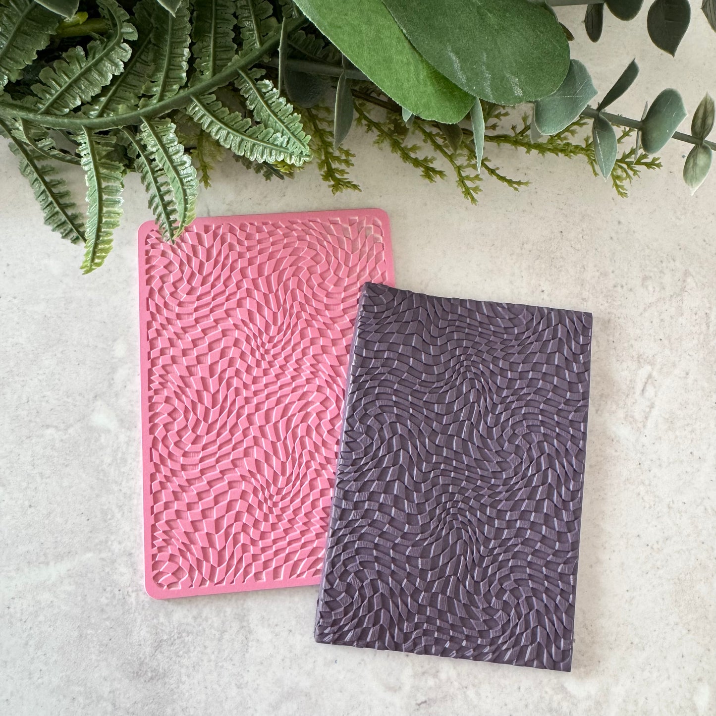 Pink and gray texture mat in the pattern of psychedelic checkerboards on a light surface with green foliage.