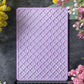 A rectangular lavender purple silicone mold with a raised geometric trellis pattern, displayed on a dark gray slate background and surrounded by yellow and pink flowers, with a ruler at the bottom showing its dimensions.