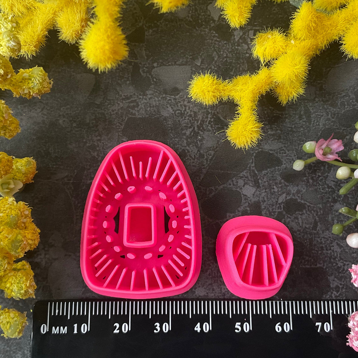 Bright pink 3d printed polymer clay cutters in bright pink and turquoise arranged on a dark textured surface, surrounded by yellow and pink flowers. Solstice Bloom Polymer Clay Cutter Set