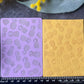 Two rectangular paper sheets with embossed pineapple patterns, one lavender purple and one golden yellow, displayed on a dark gray surface with a black measuring ruler below and yellow flowers and green leaves around the edges.