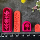 A set of 3d printed flower-shaped polymer clay cutters in different sizes arranged on a dark textured surface with a black ruler below and yellow and pink flowers around the edges. The cutters are hot pink and orange, Winter Meadow Polymer Clay Cutter Set.