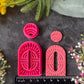 Bright pink 3d printed polymer clay cutters shaped like stylized  arch and circular figures, displayed on a dark textured surface surrounded by decorative flowers and greenery. Woven Earth Polymer Clay Cutter Set